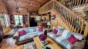 Un interno accogliente di una baita con una scala in legno, un divano, un'area pranzo e una cucina.