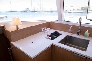 A modern kitchen with a sink, a window offering a marina view, and a small table with a lamp. - Sun-Kissed Sailing Adventure in the Ionian Islands, Lefkada (Lefkada)