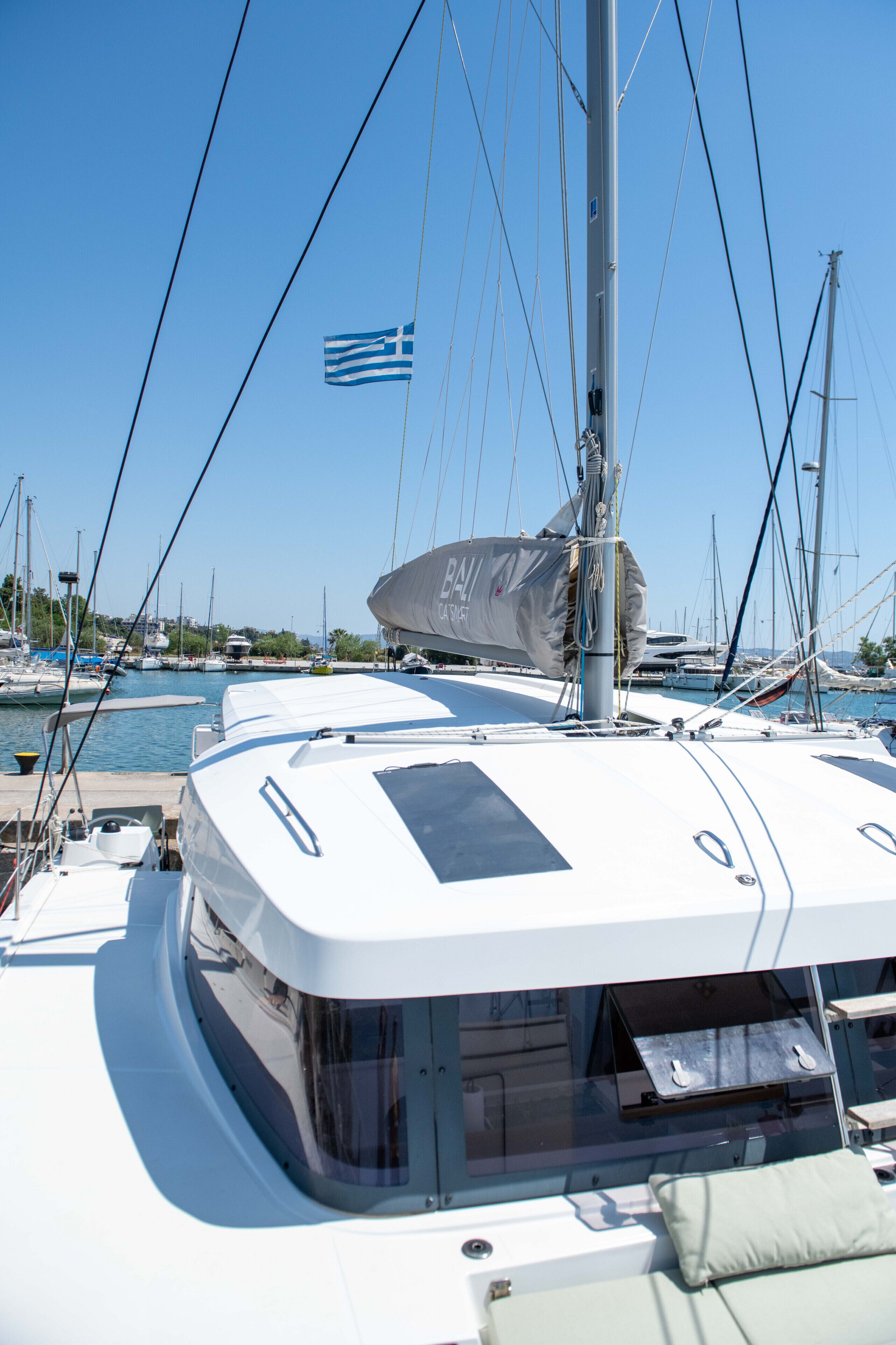 A sailboat docked at a marina with a clear sky, other boats in the background, and a flag.