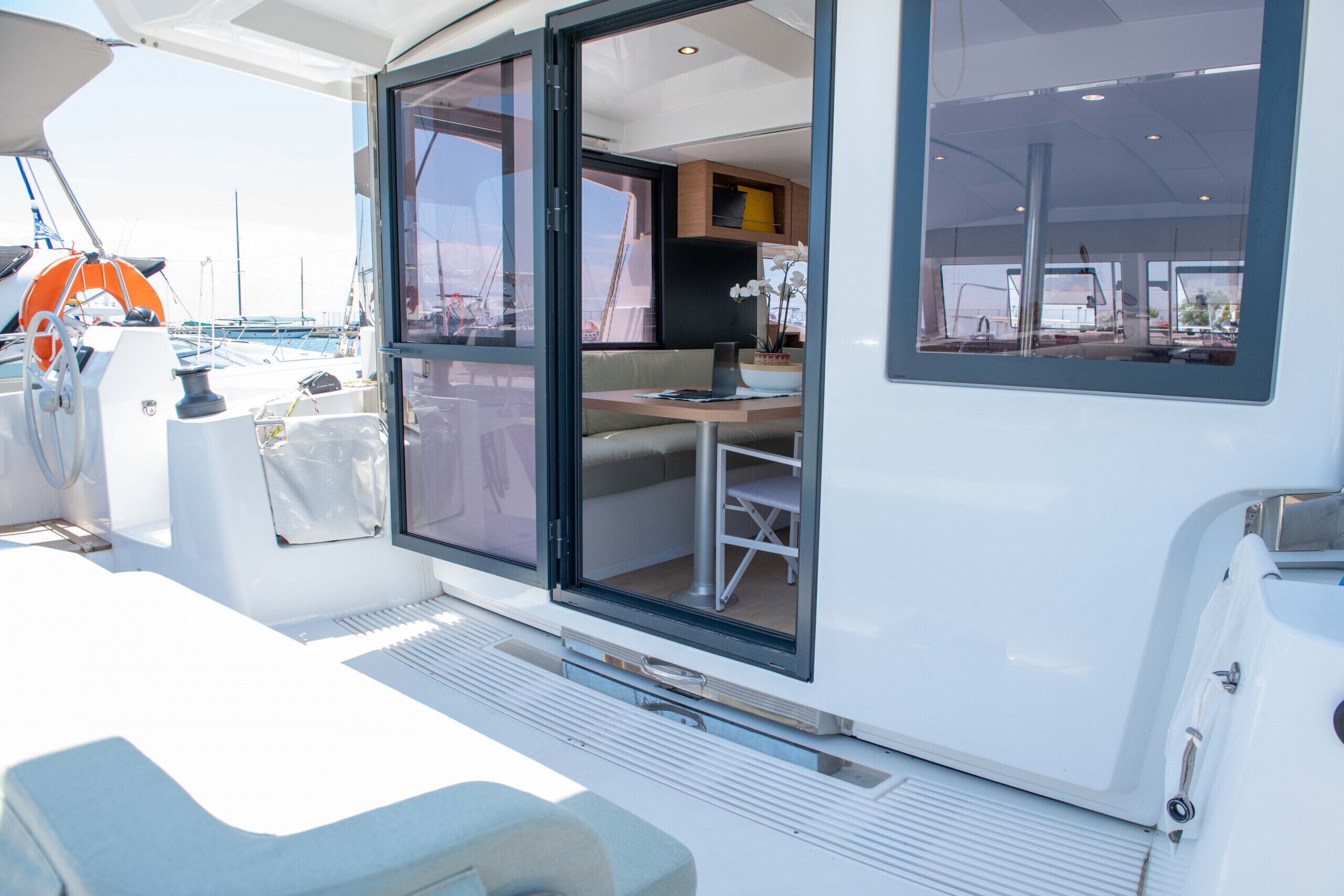 Un interior de barco moderno con comedor, cocina y ventanas amplias.