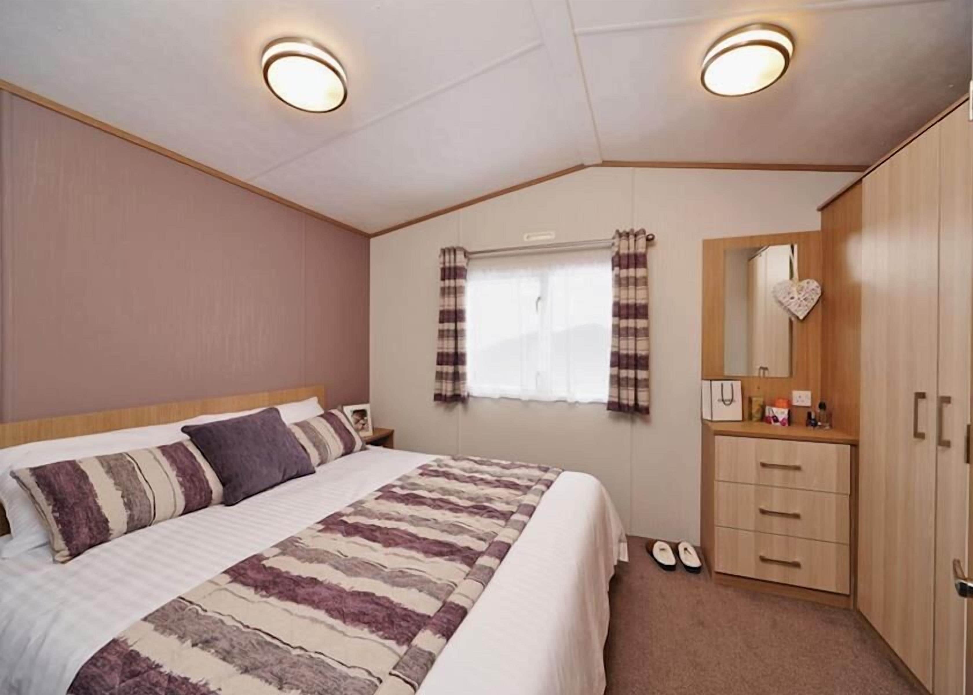 A bedroom with a bed, a dresser, a mirror, and a window with curtains.