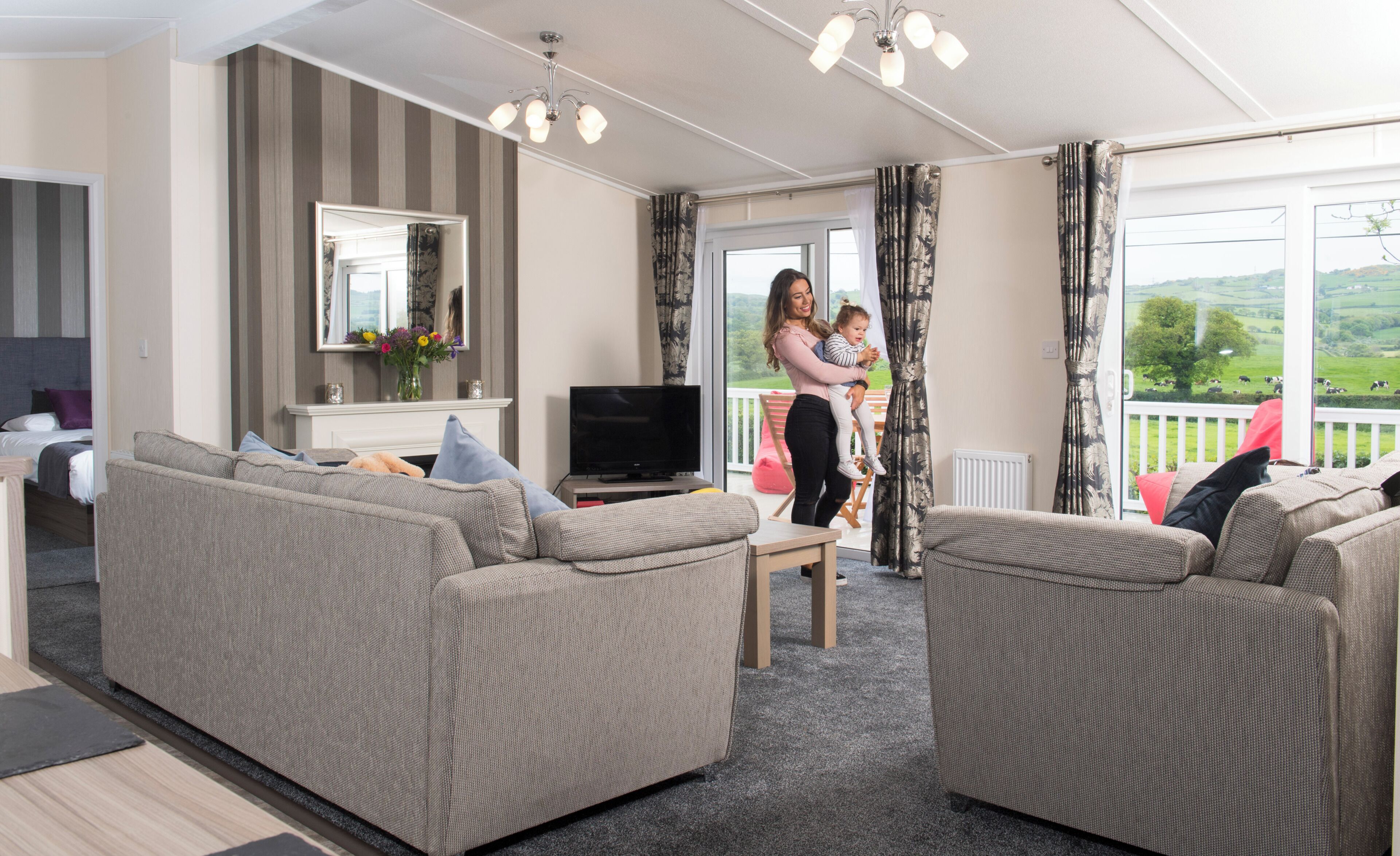A living room with sofas, a TV, and a balcony with a view of the countryside.