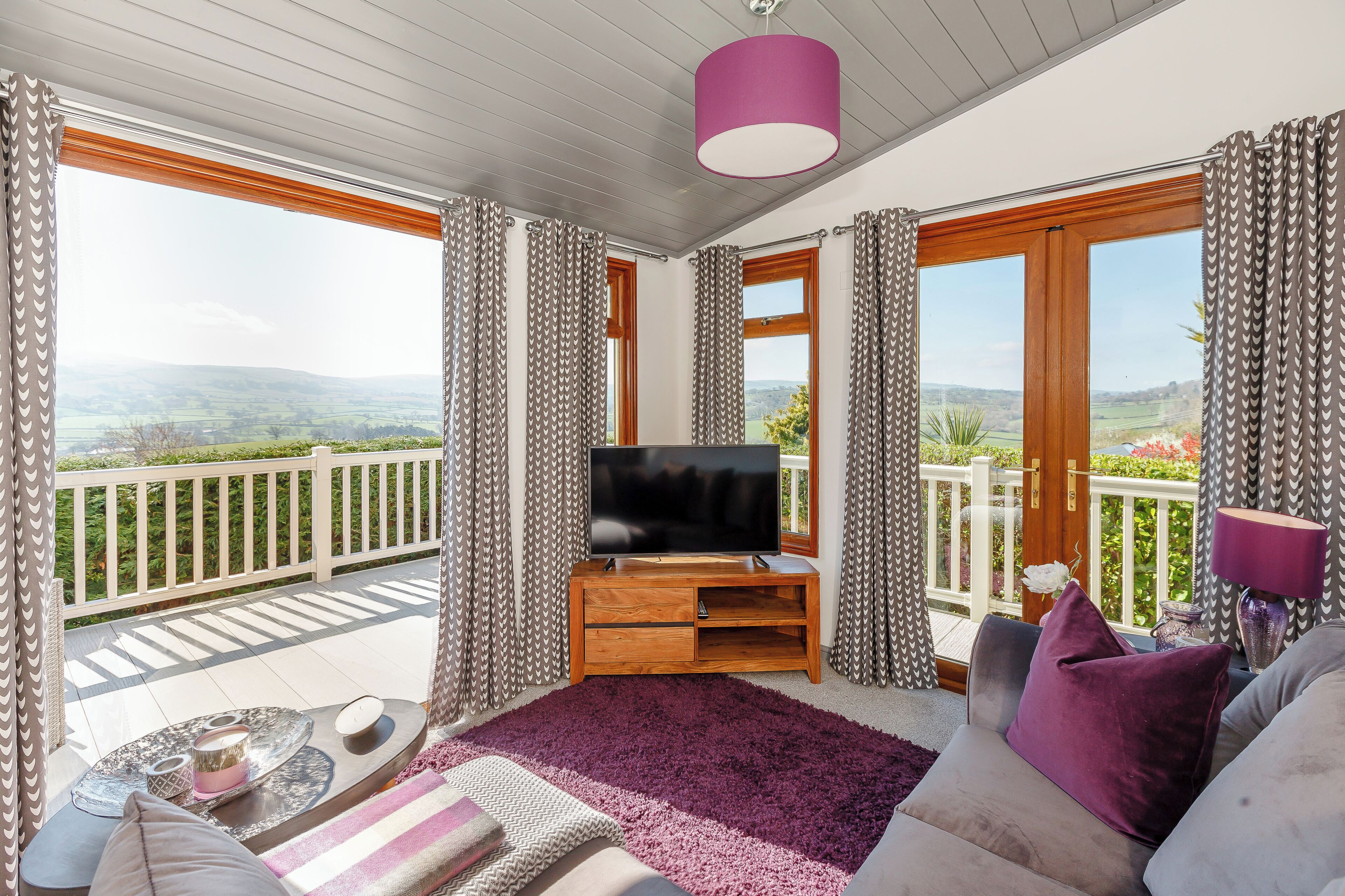 A balcony with a TV, a sofa, and a table with a rug.