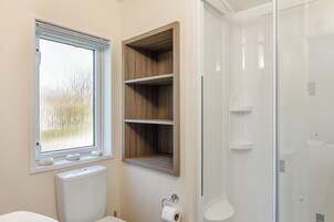 Un baño con inodoro, ventana, estante de madera y cabina de ducha de cristal.