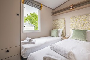 Un dormitorio con dos camas, una ventana con cortinas, una figurita de panda y un cabecero con estampado floral.