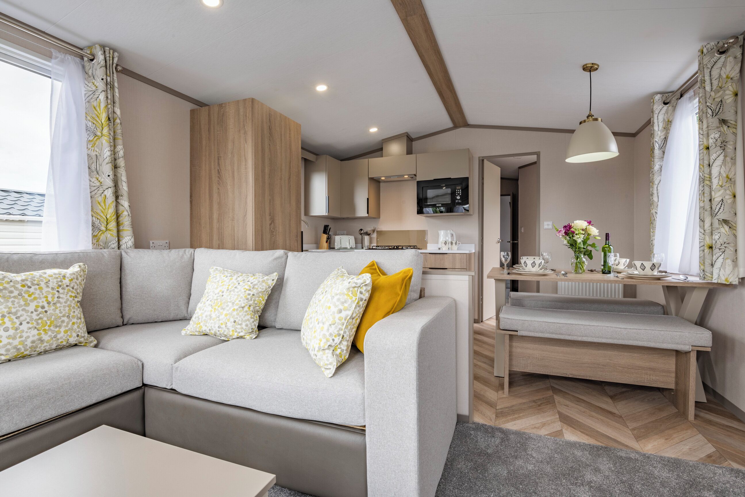 A modern living room with a sofa, a coffee table, a bench, and a kitchen area with a microwave.