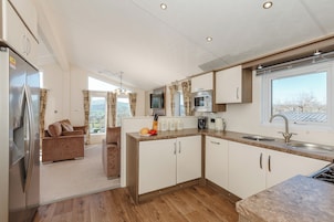 A modern kitchen with a built-in microwave, a refrigerator, and a sink. There is a sofa and a dining area visible in the background.