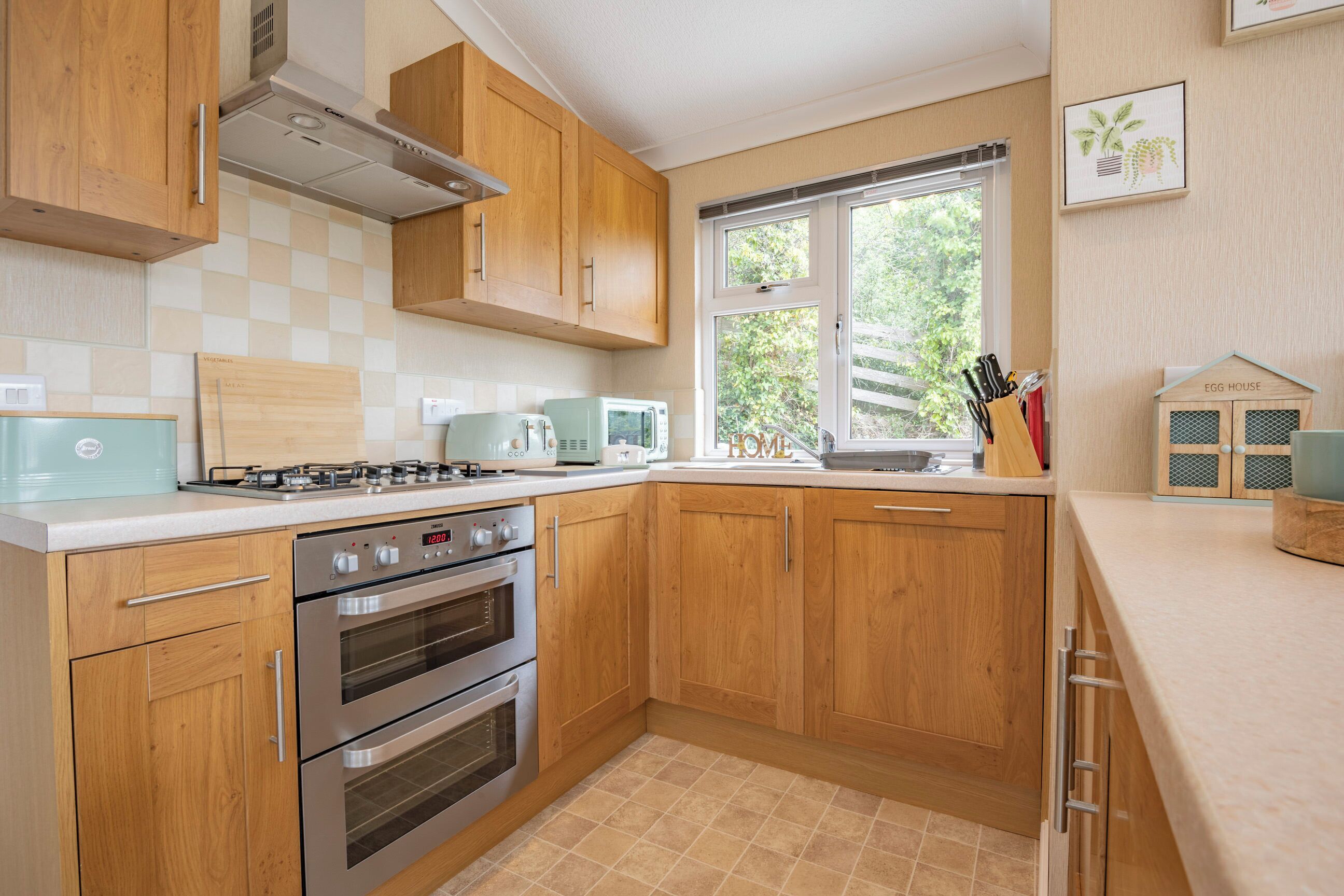 Une cuisine moderne avec des meubles en bois, des appareils en acier inoxydable et une fenêtre donnant sur un paysage verdoyant.