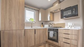 Une cuisine moderne avec des meubles en bois, un four encastré, un four à micro-ondes et une fenêtre qui laisse entrer la lumière naturelle.