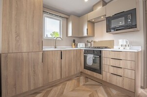 Une cuisine moderne avec des meubles en bois, un four encastré, un four à micro-ondes et une fenêtre qui laisse entrer la lumière naturelle.