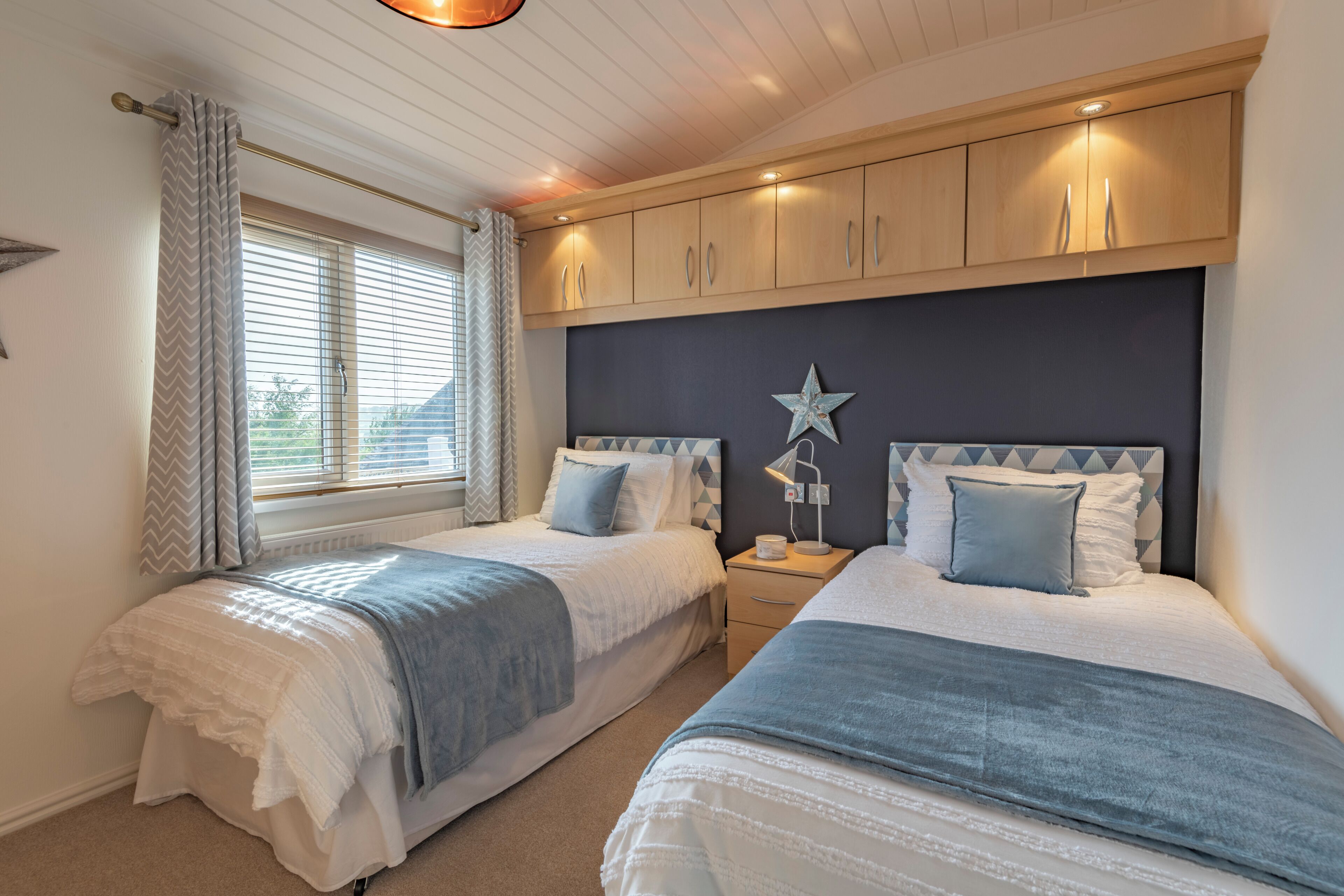 A bedroom with two beds, wooden cabinets, a star decoration, and a window with curtains.