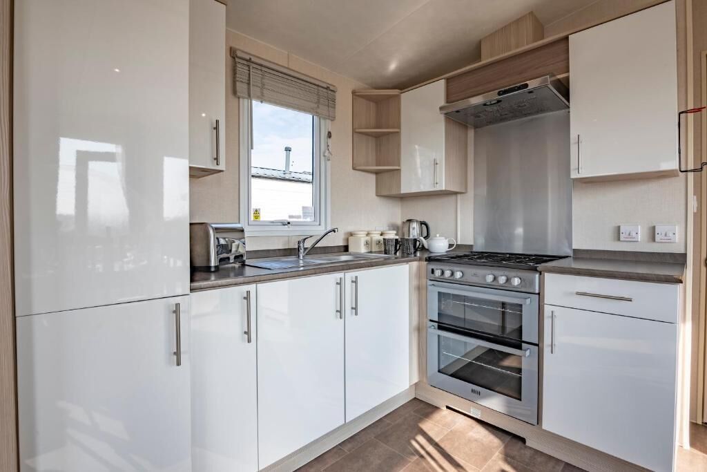 A modern kitchen with white cabinets, a stove, oven, and a window with blinds.