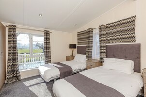 Un dormitorio con dos camas, una ventana con cortinas, una mesita de noche con lámpara y vistas al exterior.