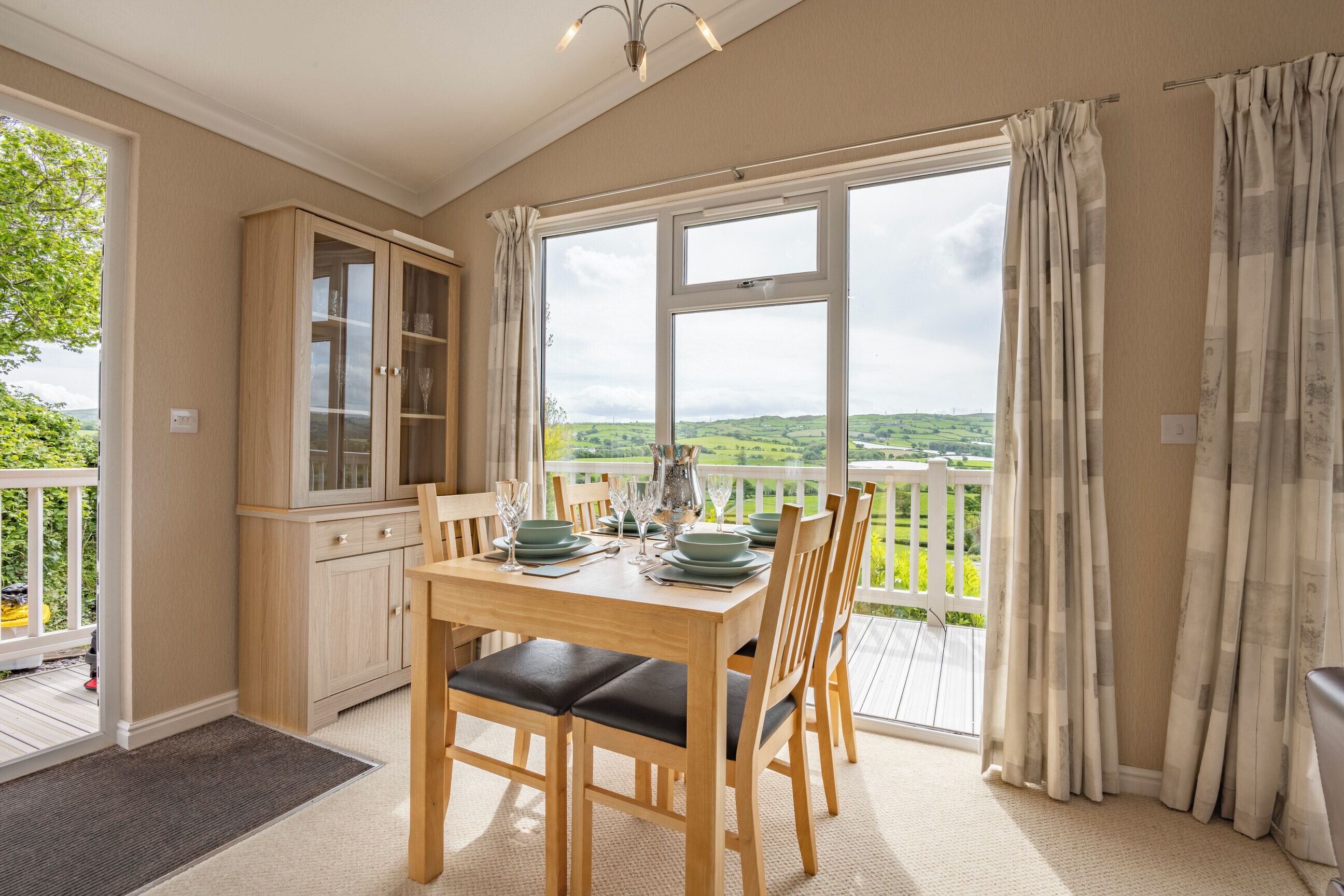 Un coin repas avec une table dressée pour quatre personnes, un buffet en bois et une vue sur un balcon doté d’une balustrade.