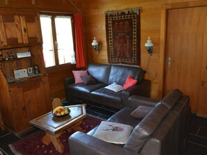 Ein gemütliches Blockhaus-Interieur mit einem Ledersofa, einem Holztisch mit Obst und einem gemusterten Teppich.