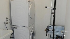 Un baño compacto con lavadora y secadora apiladas, un lavamanos y un estrecho armario alto.