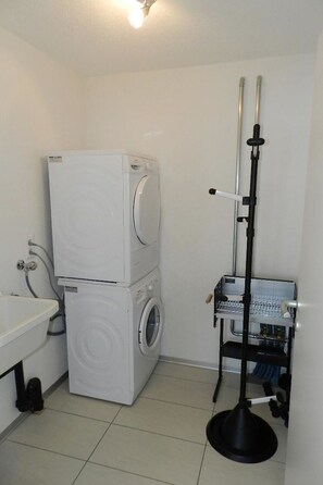 A compact bathroom with a stacked washer and dryer, a sink, and a tall, narrow shelf unit. - Schön-Egg Appartement/Fewo, Dusche, WC 2-Bettwohnung by Interhome (Zweisimmen)