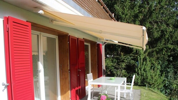 Un patio con mesa y sillas, una zona cubierta y una puerta roja.