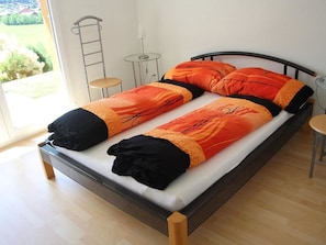 Een bed met een zwart frame, een witte matras en beddengoed in oranje en zwart. Er staan twee kleine tafels naast het bed.