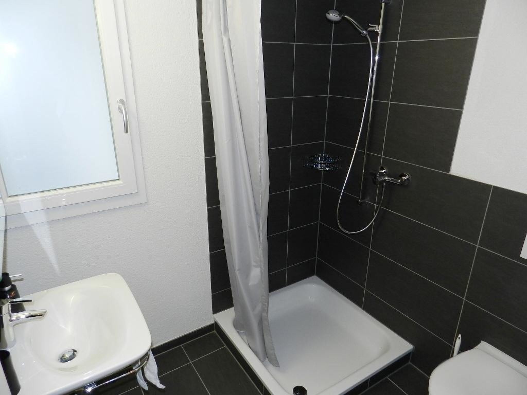 A bathroom with a white sink, a shower with a curtain, and black tiled walls.