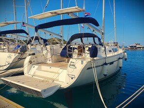Ein Segelboot liegt in einer Marina festgemacht, mit mehreren Masten und Flaggen, einer Kabine mit Fenstern und einem Deck.