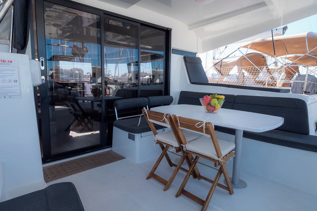 A compact, modern outdoor seating area with a table and chairs, a cushioned bench, and a glass door leading to an interior space.