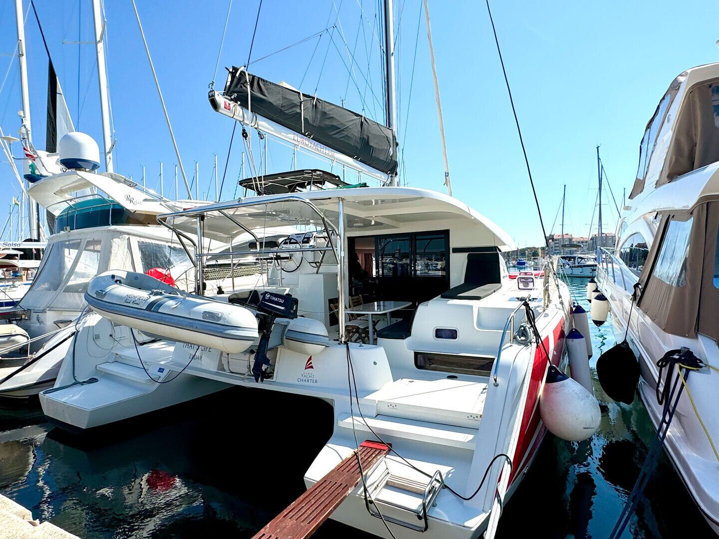 Ein Yachthafen mit einer weißen Yacht, die ein überdachtes Deck, ein Steuer und ein kleines Boot mit dem Namen 'THAI LIFE' zeigt, das daneben liegt.