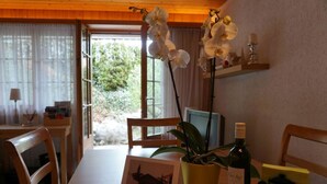 Ein Holztisch mit Stühlen, ein Blumentopf, eine Weinflasche und ein gerahmtes Bild.
