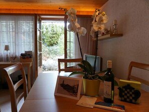 Ein Holztisch mit Stühlen, ein Blumentopf, eine Weinflasche und ein gerahmtes Bild.