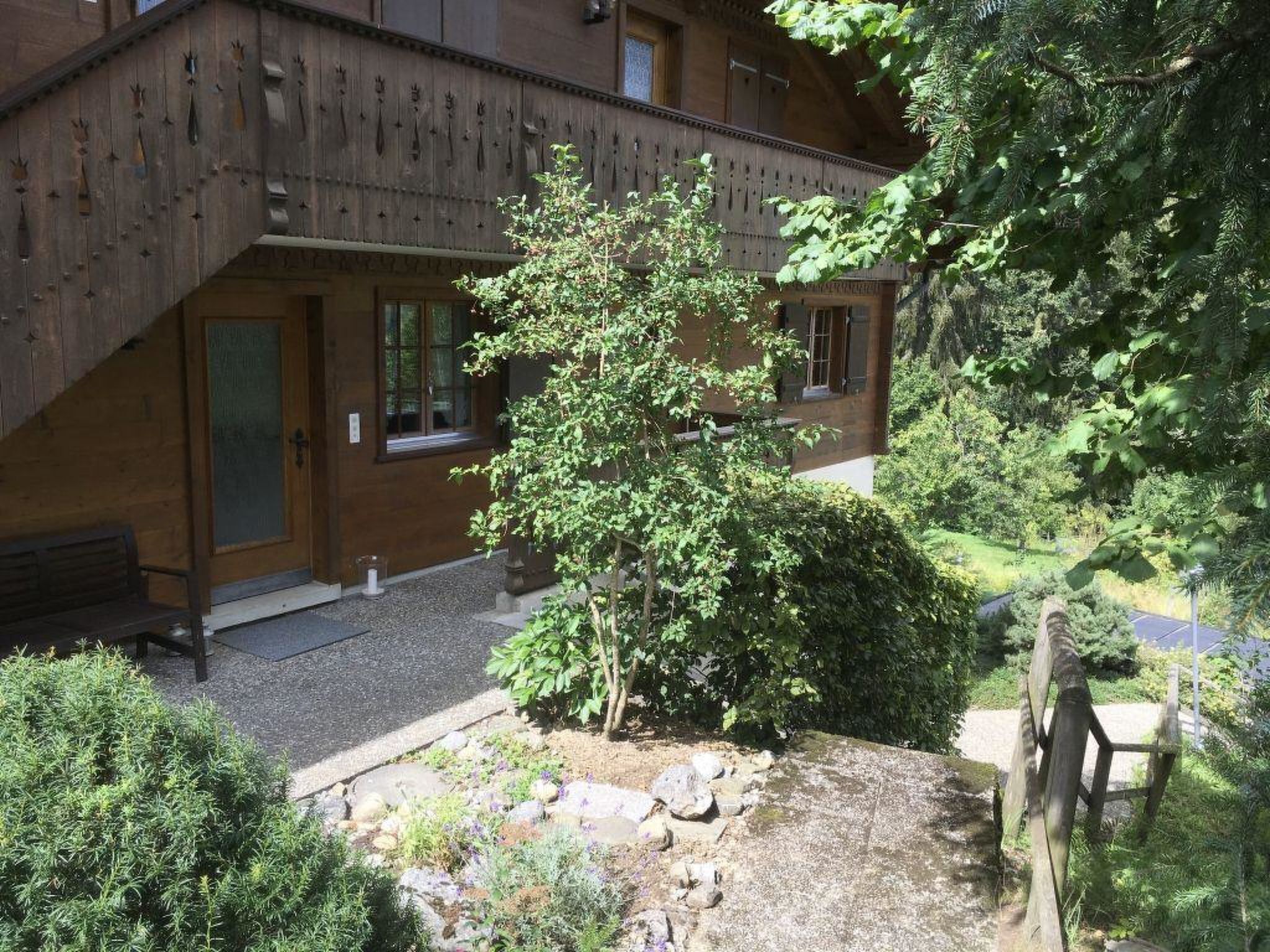 Ein Holzhaus mit Balkon, einer Bank und einem kleinen Garten mit Steinen und Pflanzen.