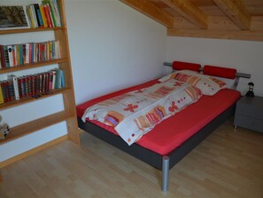 A bedroom with a bed, a nightstand, a bookshelf, and a wooden ceiling. - Alpha Appartement/Fewo, Dusche oder Bad, WC 4-Bettwohnung by Interhome (Zweisimmen)