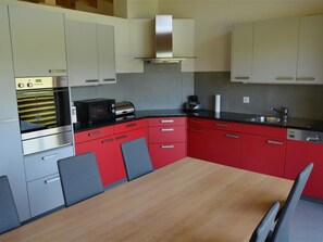 A modern kitchen with stainless steel appliances, red cabinetry, and a wooden dining table. - Alpha Appartement/Fewo, Dusche oder Bad, WC 4-Bettwohnung by Interhome (Zweisimmen)