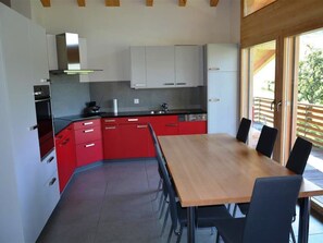 A modern kitchen with red cabinets, a wooden dining table, and a view of the outdoors.