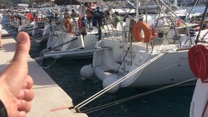 A marina with boats docked, a person giving a thumbs-up, and a lifebuoy on a boat. - Sun-Kissed Sailing Adventure in the Serene Saronic Islands (Elefsina)