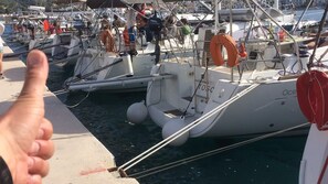 Ein Yachthafen mit vertäuten Booten, eine Person zeigt Daumen hoch und ein Rettungsring auf einem Boot.