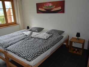 Ein Schlafzimmer mit Bett, Kissen, einem Nachttisch, einem Gemälde und einem Fenster.
