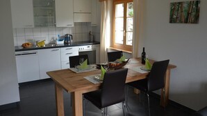 Une cuisine de taille réduite avec des meubles blancs, une table à manger avec des chaises et une fenêtre agrémentée de rideaux.