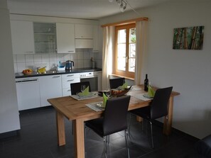 Eine kleine Küche mit weißen Schränken, einem Esstisch mit Stühlen und einem Fenster mit Vorhängen.
