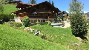 Un grand chalet en bois doté de nombreux balcons, entouré d’une végétation luxuriante et surplombant un ciel dégagé.