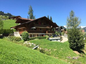Eine große Holchhütte mit mehreren Balkonen, umgeben von üppigem Grün und blauem Himmel.