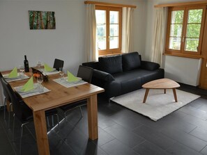 A modern living room with a dining table, black leather sofa, and a wooden coffee table. - Bijou Eggetli Appartement/Fewo, Dusche oder Bad, WC 2-Bettwohnung by Interhome (Zweisimmen)