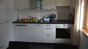 Une cuisine de taille réduite avec des meubles blancs, un lave-vaisselle, une machine à café et une fenêtre avec des rideaux.