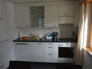 Eine kompakte Küche mit weißen Schränken, einem Geschirrspüler, einer Kaffeemaschine und einem Fenster mit Vorhängen.