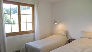 Una habitación con dos camas, una ventana y una mesita de noche con lámpara.