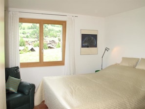 A bedroom with a bed, a chair, a window with a view of houses, and a lamp. - Grüenbüelti Appartement/Fewo, Dusche oder Bad, WC 6-Bettwohnung by Interhome (Gstaad)