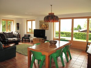 A spacious living room with a wooden dining table, green chairs, a sofa, and a television. - Grüenbüelti Appartement/Fewo, Dusche oder Bad, WC 6-Bettwohnung by Interhome (Gstaad)