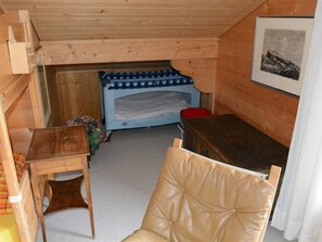 A small, cozy room with a wooden bunk bed, a small table, a chair, and a framed picture on the wall.