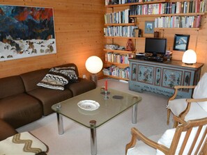 Un salon chaleureux avec un canapé marron, une table basse en verre et un meuble en bois rempli de livres.
