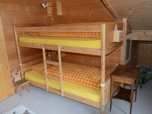 A bunk bed with a small chair and a table in a wooden room.