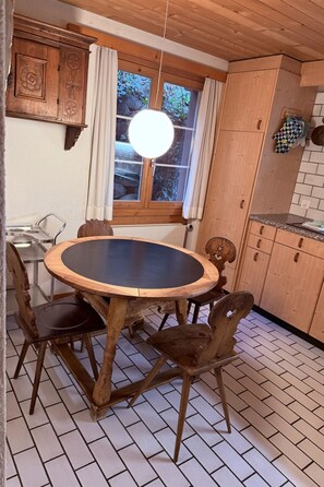 Ein Holztisch mit Stühlen, ein Fenster mit Vorhängen und ein Küchenbereich mit Schränken.